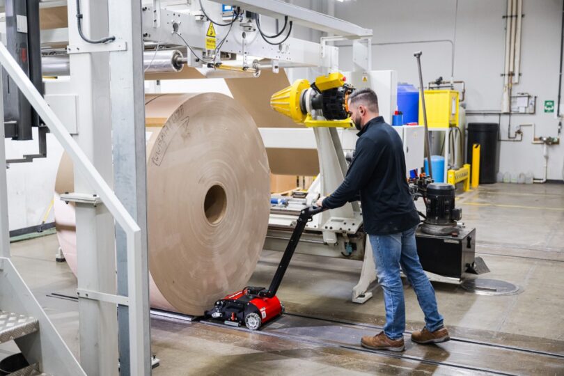 Worker using PowerPusher to load a large paper roll onto an unwinder machine in a paper converting facility