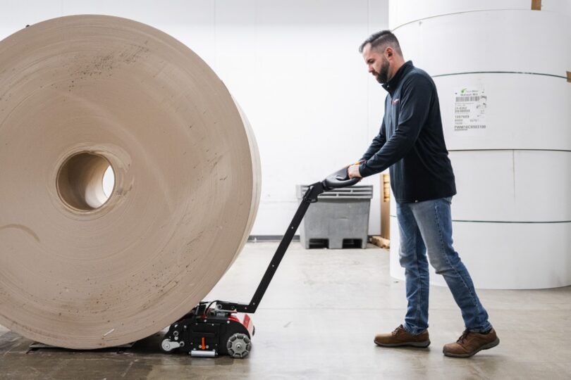 Worker using PowerPusher to easily move a massive paper roll in a paper mill warehouse