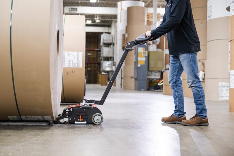 Operator maneuvering a heavy paper roll with the PowerPusher electric roll pusher in an industrial warehouse