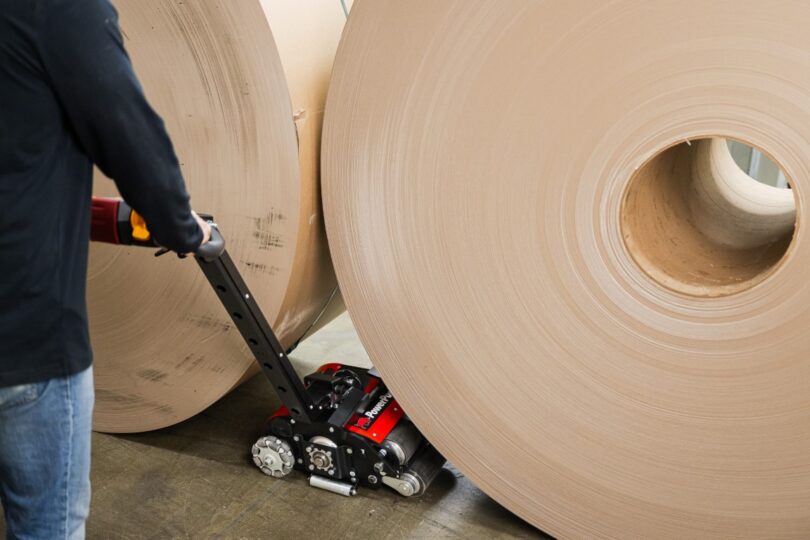 Close-up of PowerPusher maneuvering between two massive paper rolls, showcasing its compact footprint for tight spaces
